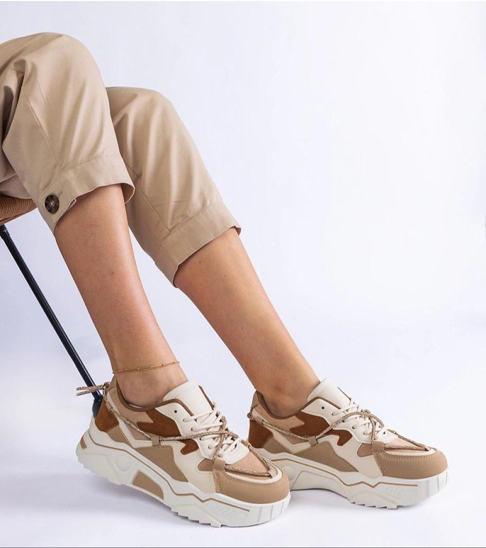 Woman wearing beige camouflage sneakers with white soles, paired with rolled-up khaki pants, sitting on a chair.
