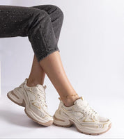 Woman wearing white chunky sole sneakers with gray soles, styled in dark speckled pants seated against a white background.