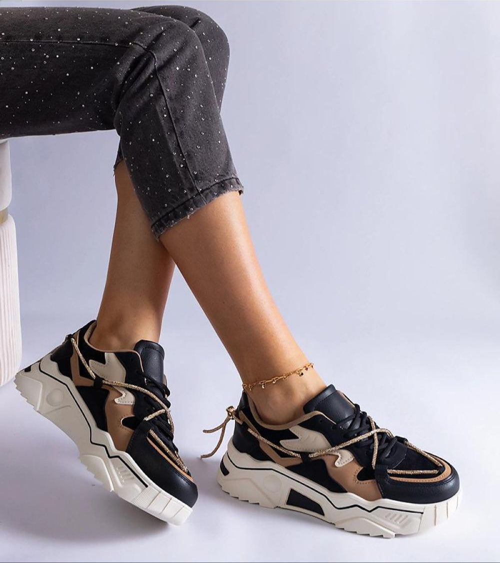 Fashionable two-tone sneakers with chunky white soles worn by a person in black speckled pants seated on a white chair.