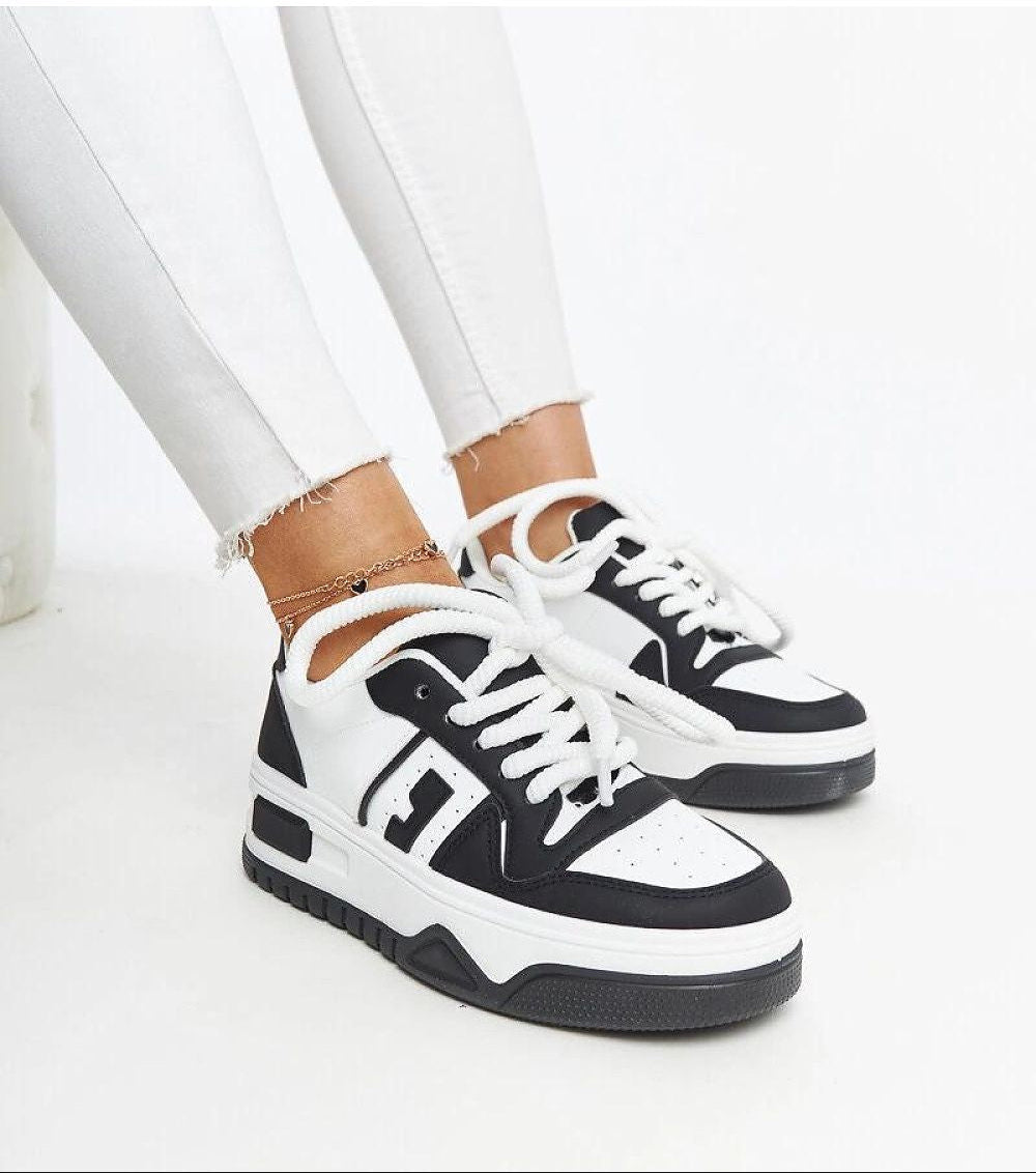 Person wearing Noira platform sneakers in black-and-white eco-leather with thick soles, showcasing modern design and comfort.