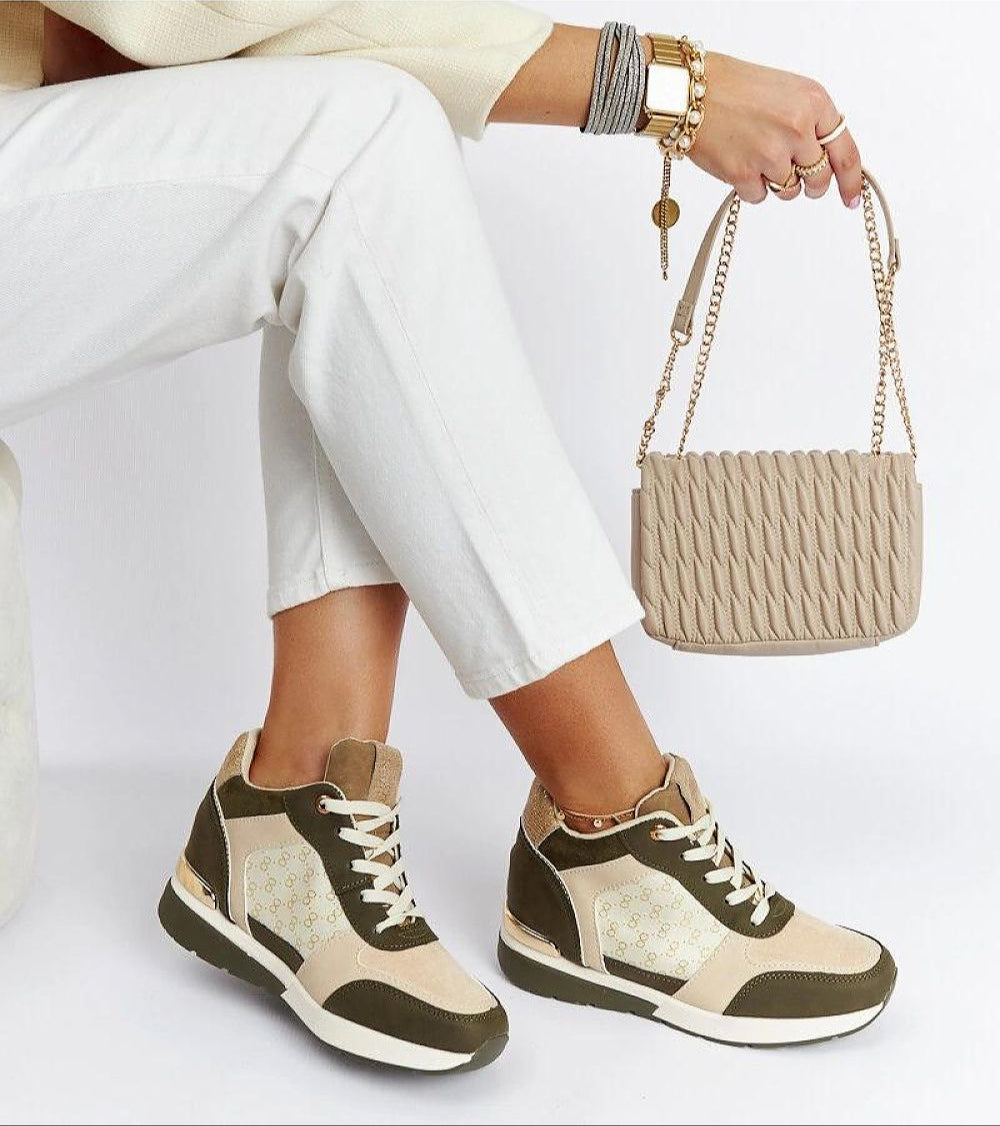 Woman showcasing stylish sneakers with olive and beige accents, paired with a chic knit-texture handbag and white pants.