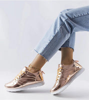 Person wearing Quirayne golden low-top sneakers with blue jeans, showcasing the shiny finish and white rubber sole.