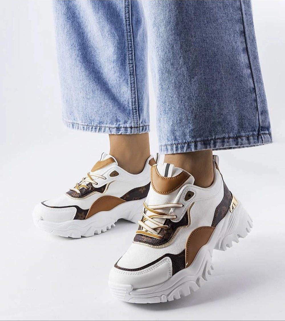 Woman wearing stylish white and brown sneakers with chunky soles, blue jeans visible above the shoes, showcasing modern design.