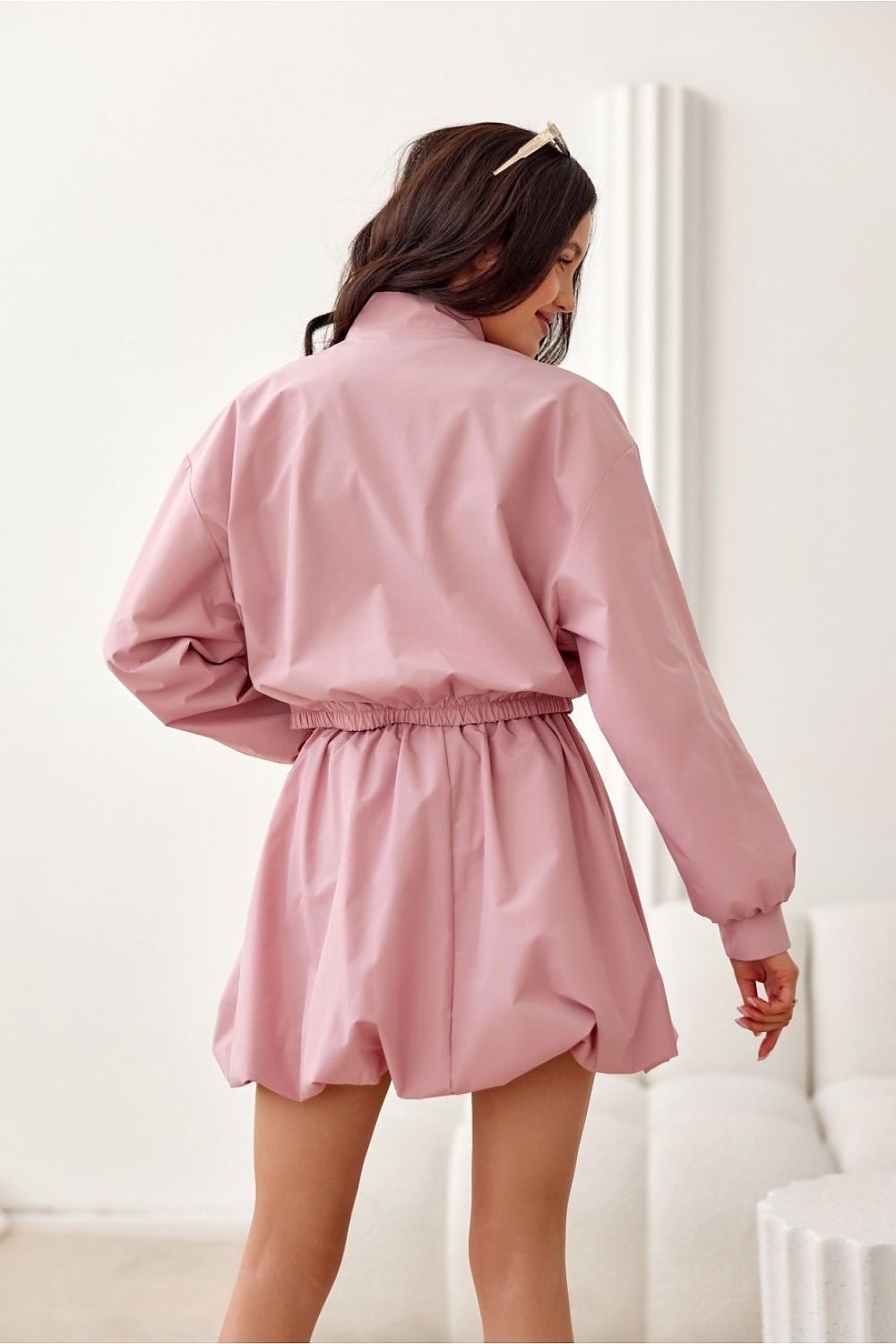 Back view of woman wearing pink lined bomber jacket with elastic waistband, showcasing modern casual style.