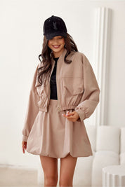 Woman wearing a beige Valserra lined bomber jacket with casual style, paired with a cap, in a minimalistic indoor setting.