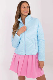 Woman wearing Morvianne Quilted Zip-Front Jacket in light blue, showcasing its sleek design and zippered pockets, paired with a pink skirt.
