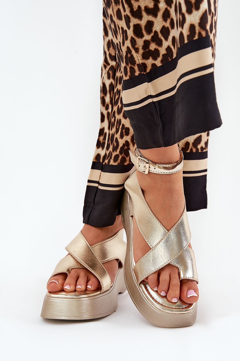 Woman wearing gold Lirianne Platform Buckle Sandals with wedge platform and leopard print pants.