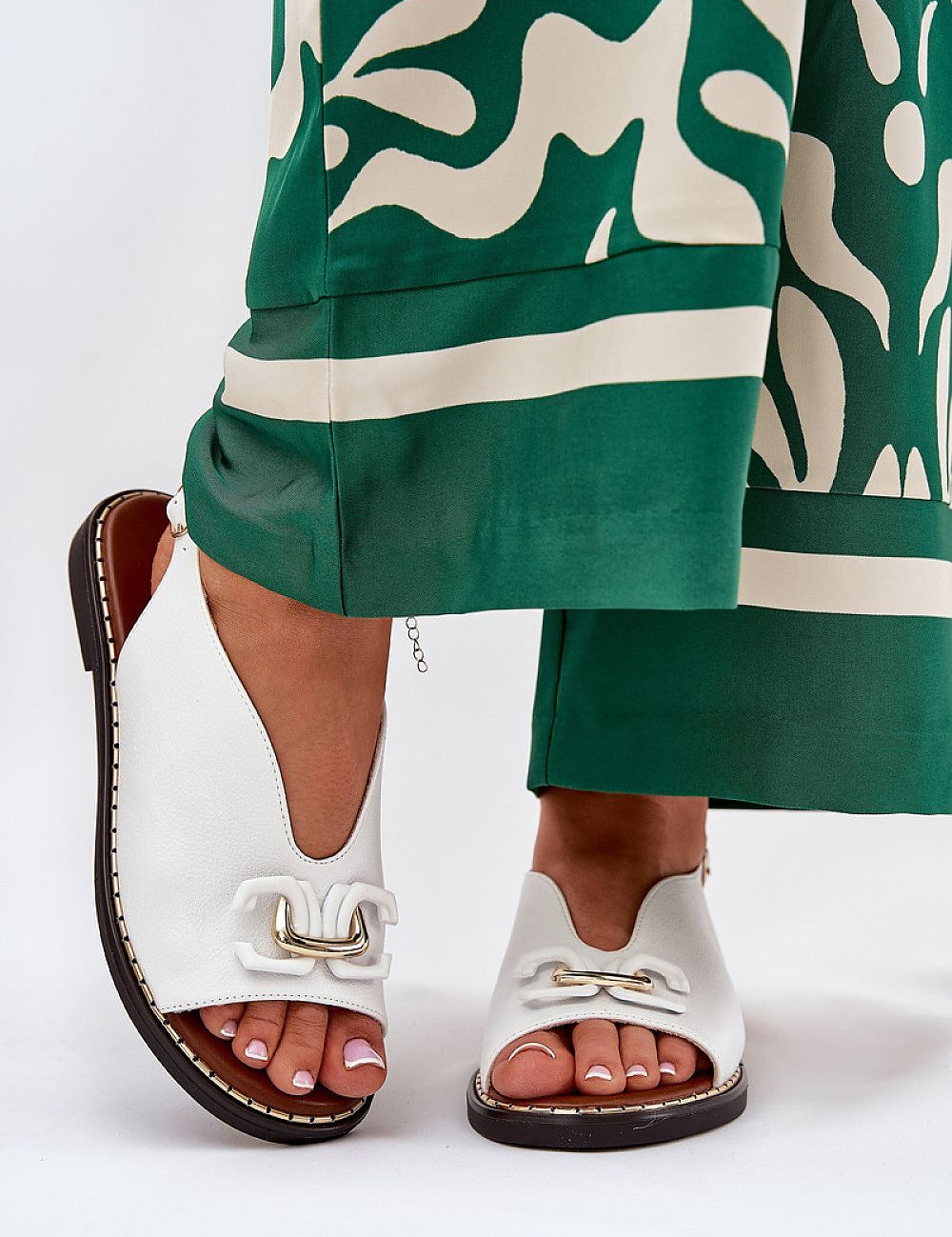 Almira flat eco-leather sandals with decorative front detail and adjustable buckle, paired with green patterned trousers.