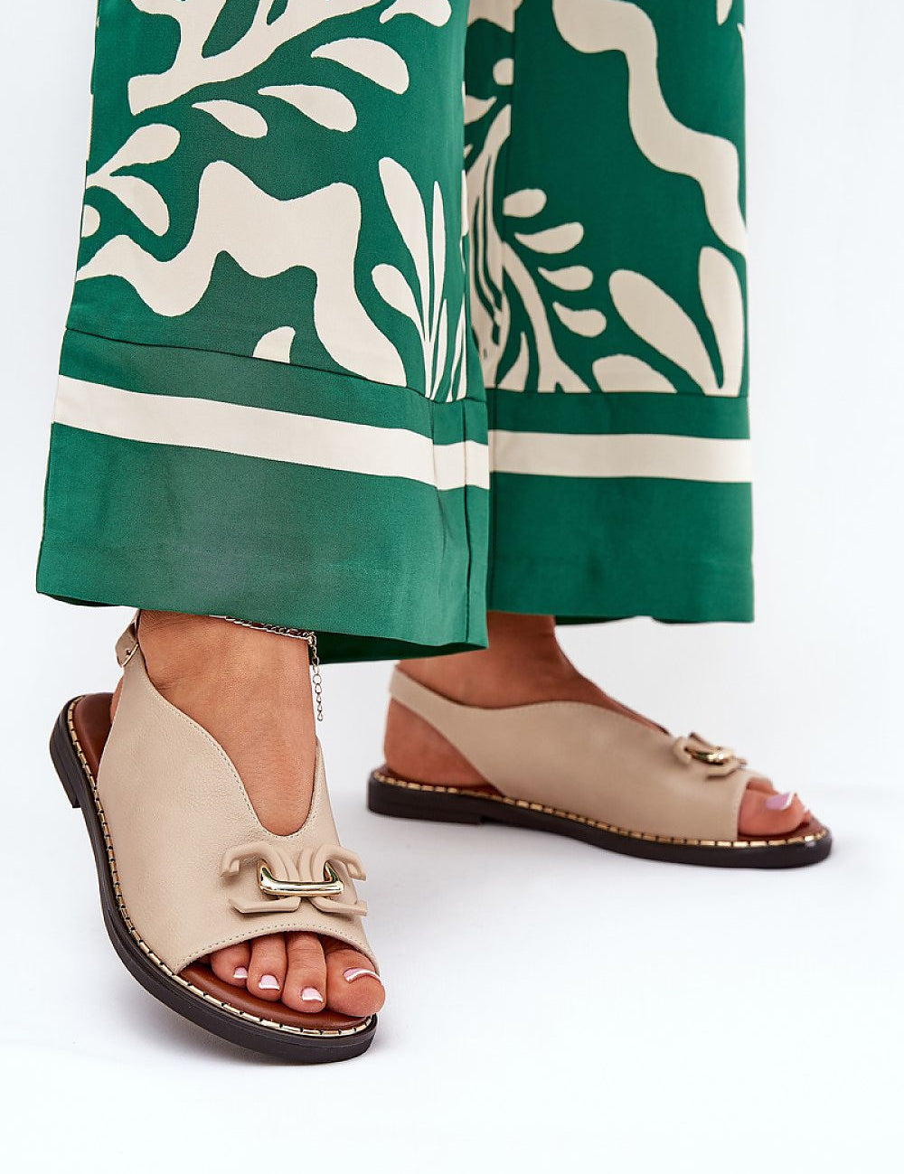 Woman wearing Almira Flat Eco-Leather Sandals with elegant design and subtle decorative front detail, paired with green patterned trousers.