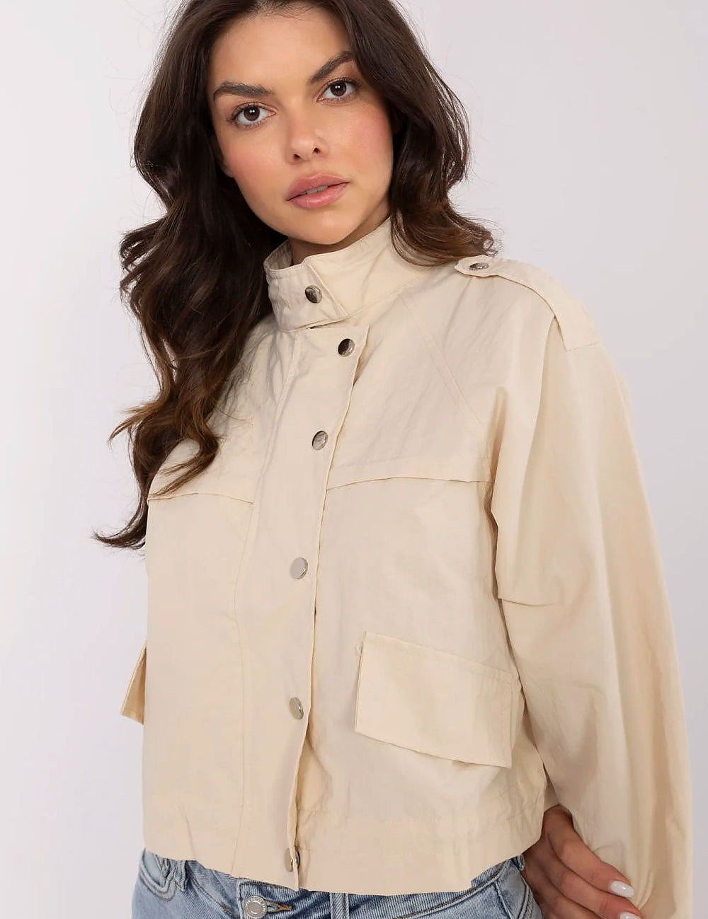 Woman wearing Corvaline Lightweight Windbreaker Jacket in beige, featuring snap-button placket and epaulets, paired with denim jeans.