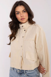 Woman wearing Corvaline Lightweight Windbreaker Jacket in beige, featuring snap-button placket and epaulets, paired with denim jeans.