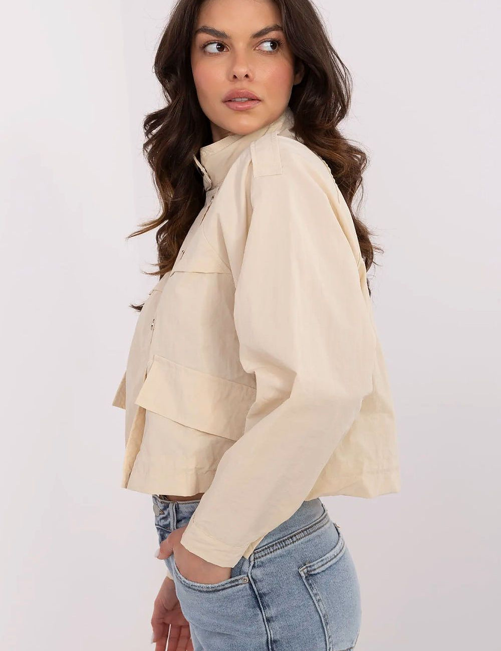Woman wearing Corvaline lightweight windbreaker jacket in beige, side view, styled with blue jeans.