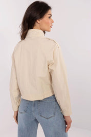 Woman wearing beige Corvaline Lightweight Windbreaker Jacket, showcasing back view with epaulets, paired with blue jeans.