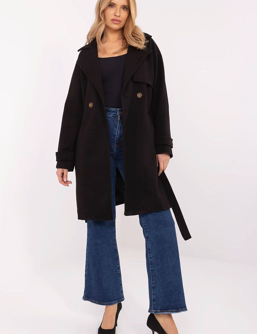 Woman wearing Corvanne double-breasted belted coat in black, styled with blue jeans and black heels for a chic, modern look.