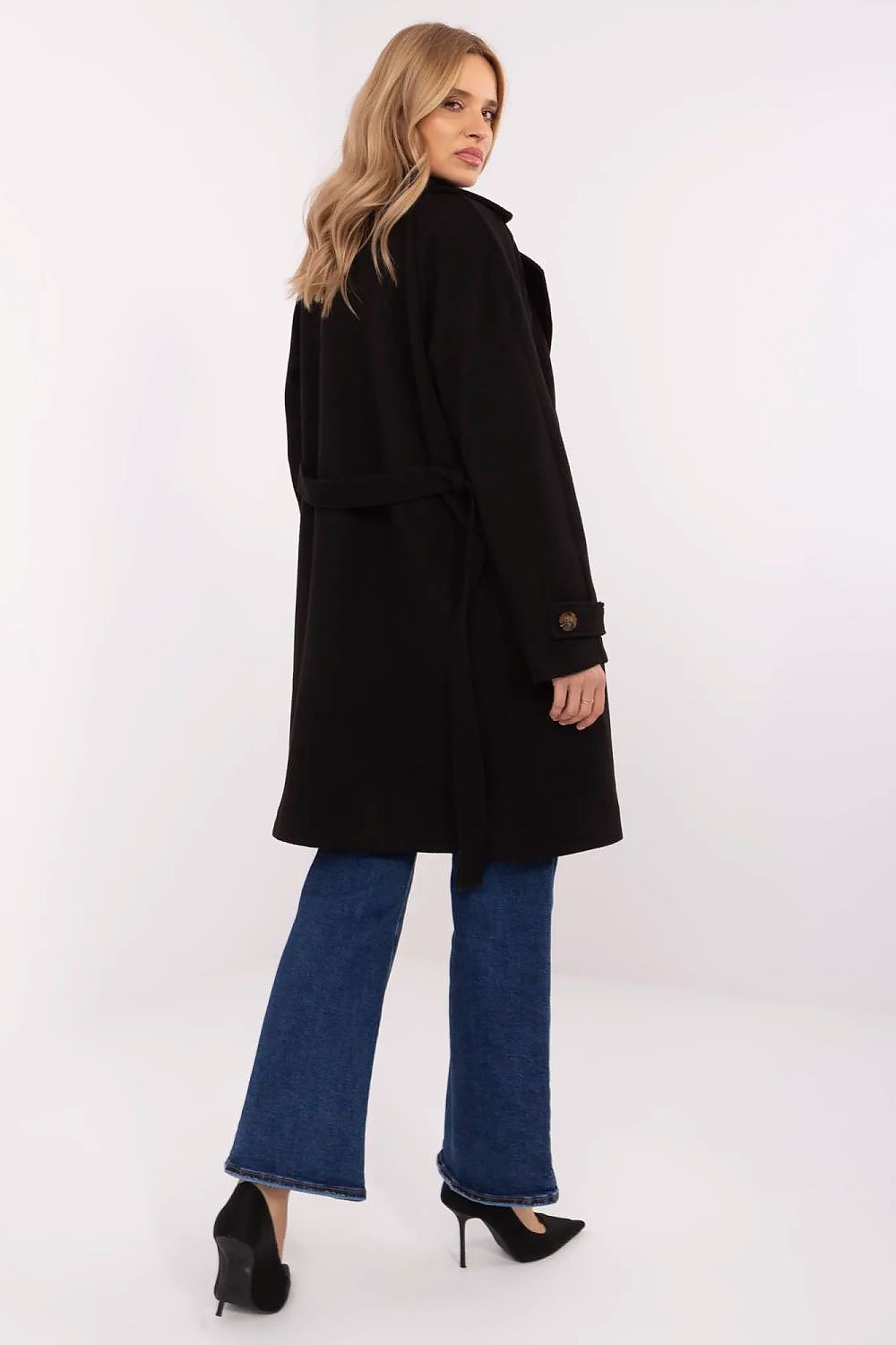 Back view of woman wearing a Corvanne Double-Breasted Belted Coat, knee-length black coat with matching waist tie, styled with jeans and heels.