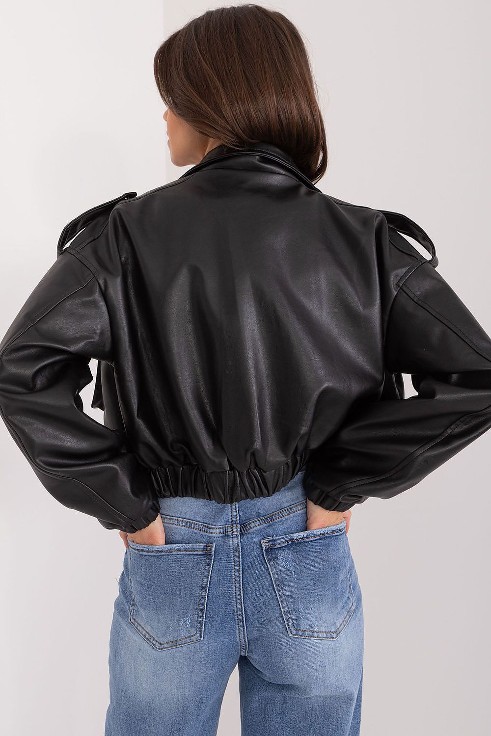 Back view of a person wearing an Arvenique Eco-Leather Short Jacket with jeans, featuring shoulder epaulettes and long sleeves.