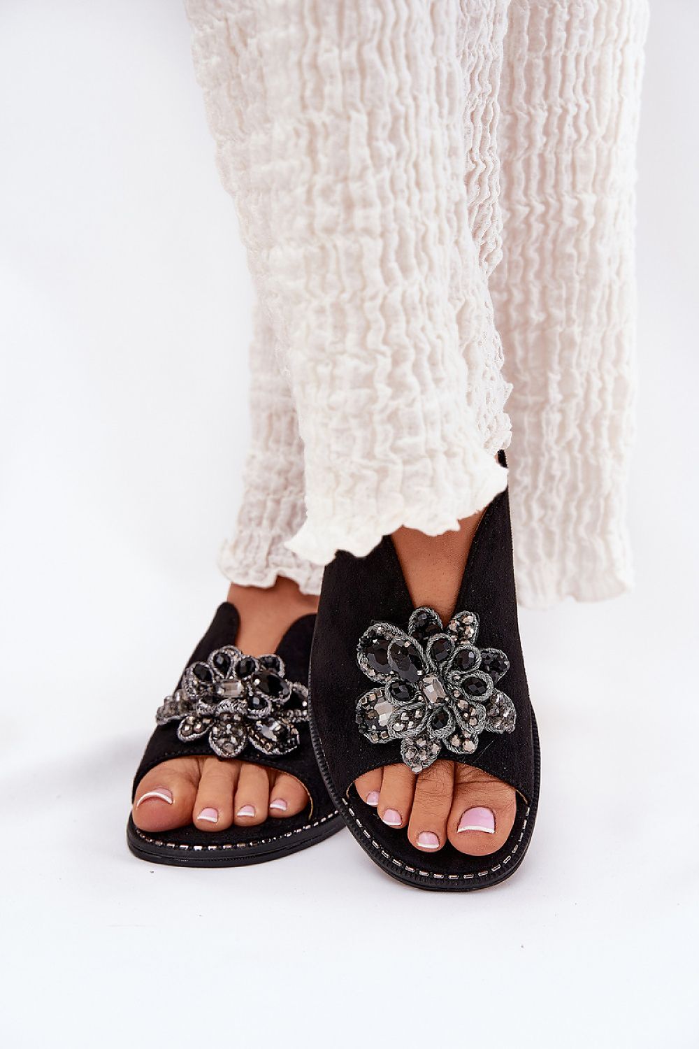 Fiorenna flat suede flower sandals with sculpted flower accent and cushioned insole, paired with flowing light fabric trousers.