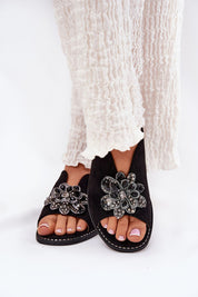 Fiorenna flat suede flower sandals with sculpted flower accent and cushioned insole, paired with flowing light fabric trousers.