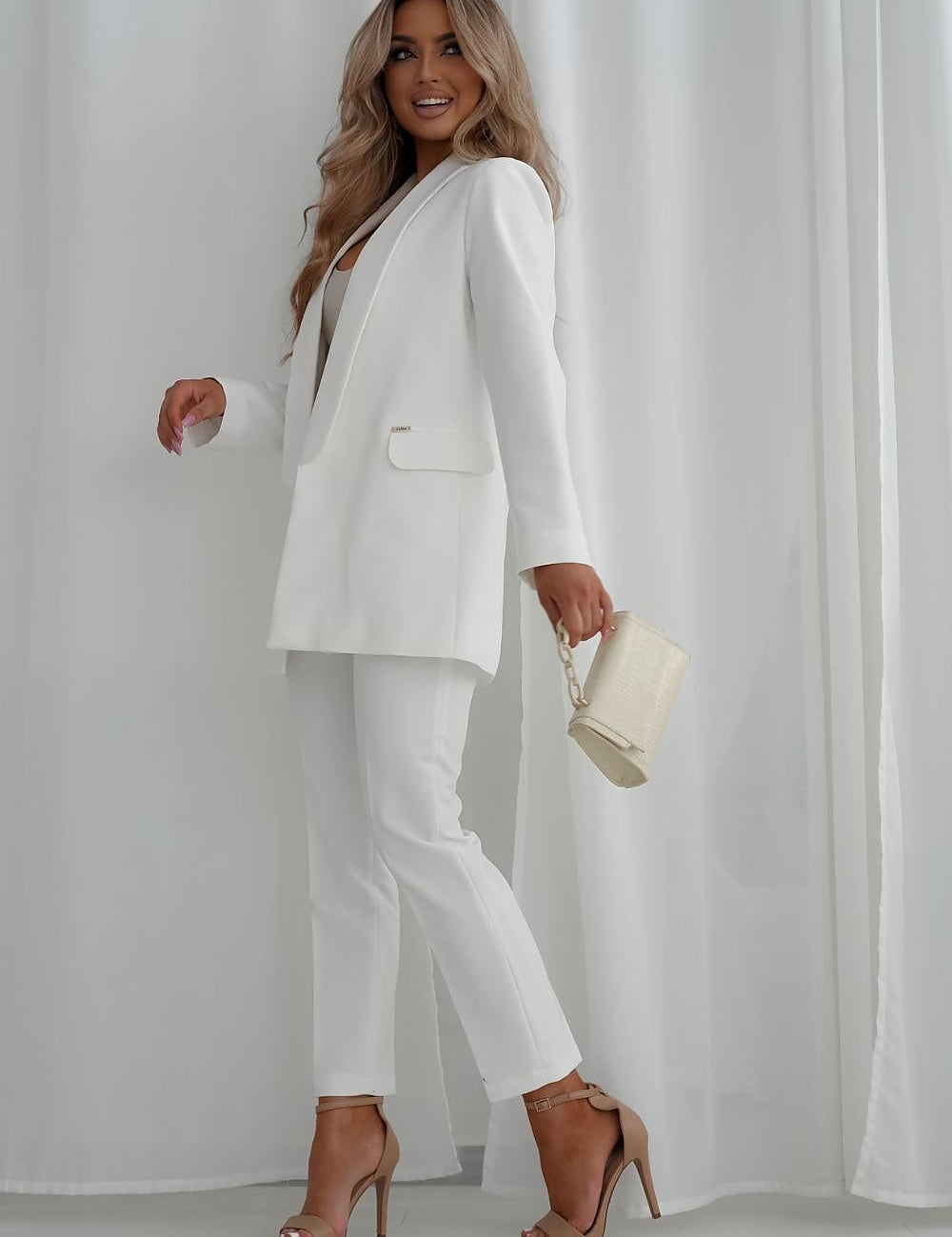8 length white trousers and blazer, holding a purse, showcasing a chic and elegant outfit.