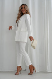 Woman wearing stylish 7/8 length white trousers and blazer, holding a purse, showcasing a chic and elegant outfit.