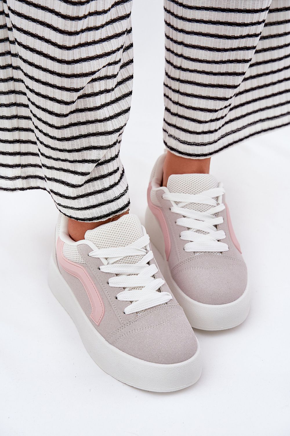 Woman wearing Ravelin suede platform sneakers with soft eco-suede and a supportive sole, styled with striped trousers for a chic look.
