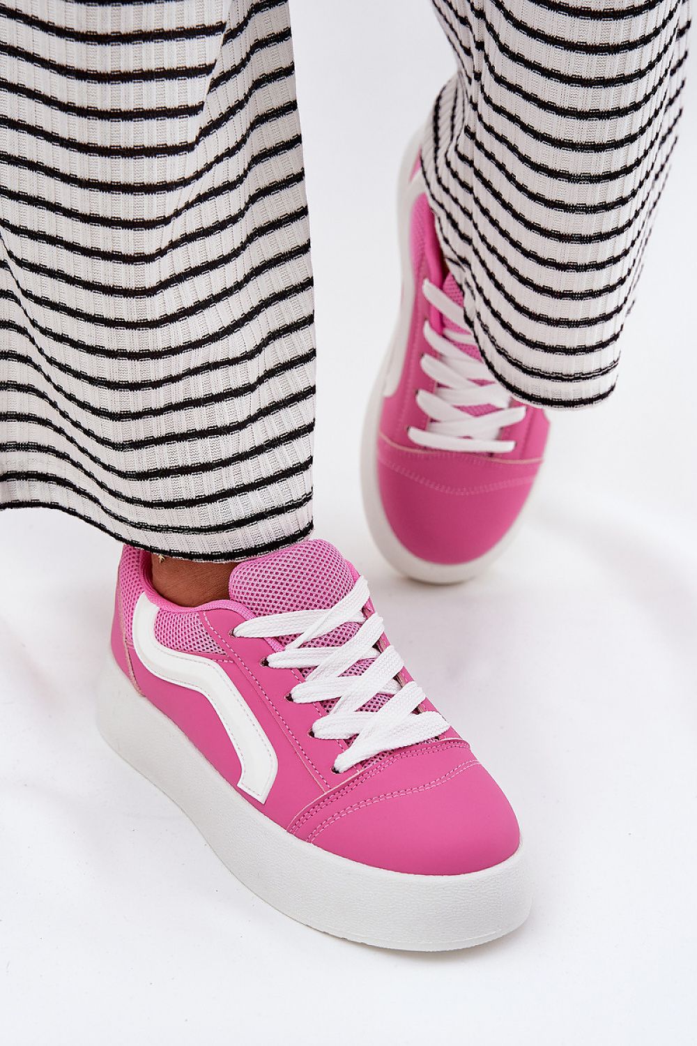 Woman wearing pink Ravelin Suede Platform Sneakers with a striped skirt, showcasing the eco-suede design and supportive platform sole.
