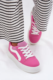 Woman wearing pink Ravelin Suede Platform Sneakers with a striped skirt, showcasing the eco-suede design and supportive platform sole.