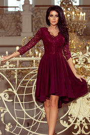 Woman wearing Nivelle Burgundy Lace High-Low Dress with lace bodice and asymmetrical hem, standing elegantly on ornate balcony.