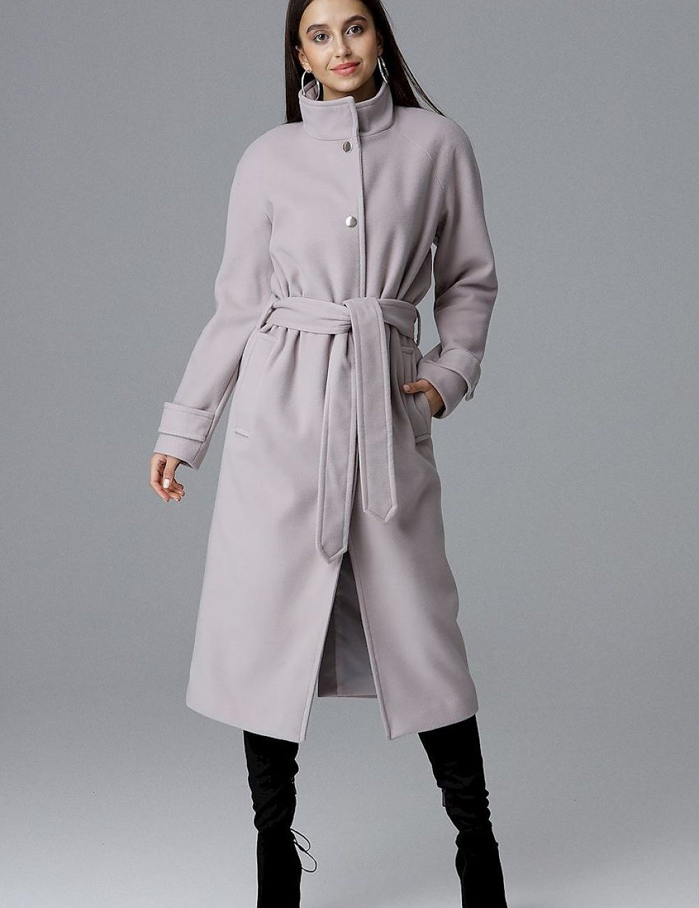 A woman wearing a Melvarine long single-breasted belted coat, featuring a timeless design with discreet pockets and a back slit.
