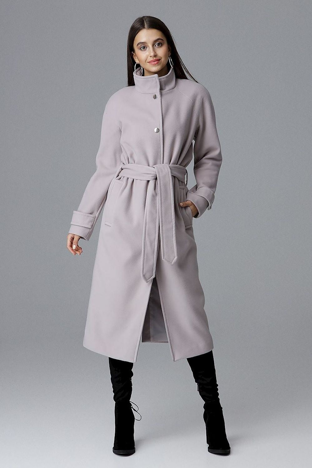 A woman wearing a Melvarine long single-breasted belted coat, featuring a timeless design with discreet pockets and a back slit.