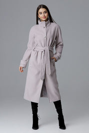 A woman wearing a Melvarine long single-breasted belted coat, featuring a timeless design with discreet pockets and a back slit.
