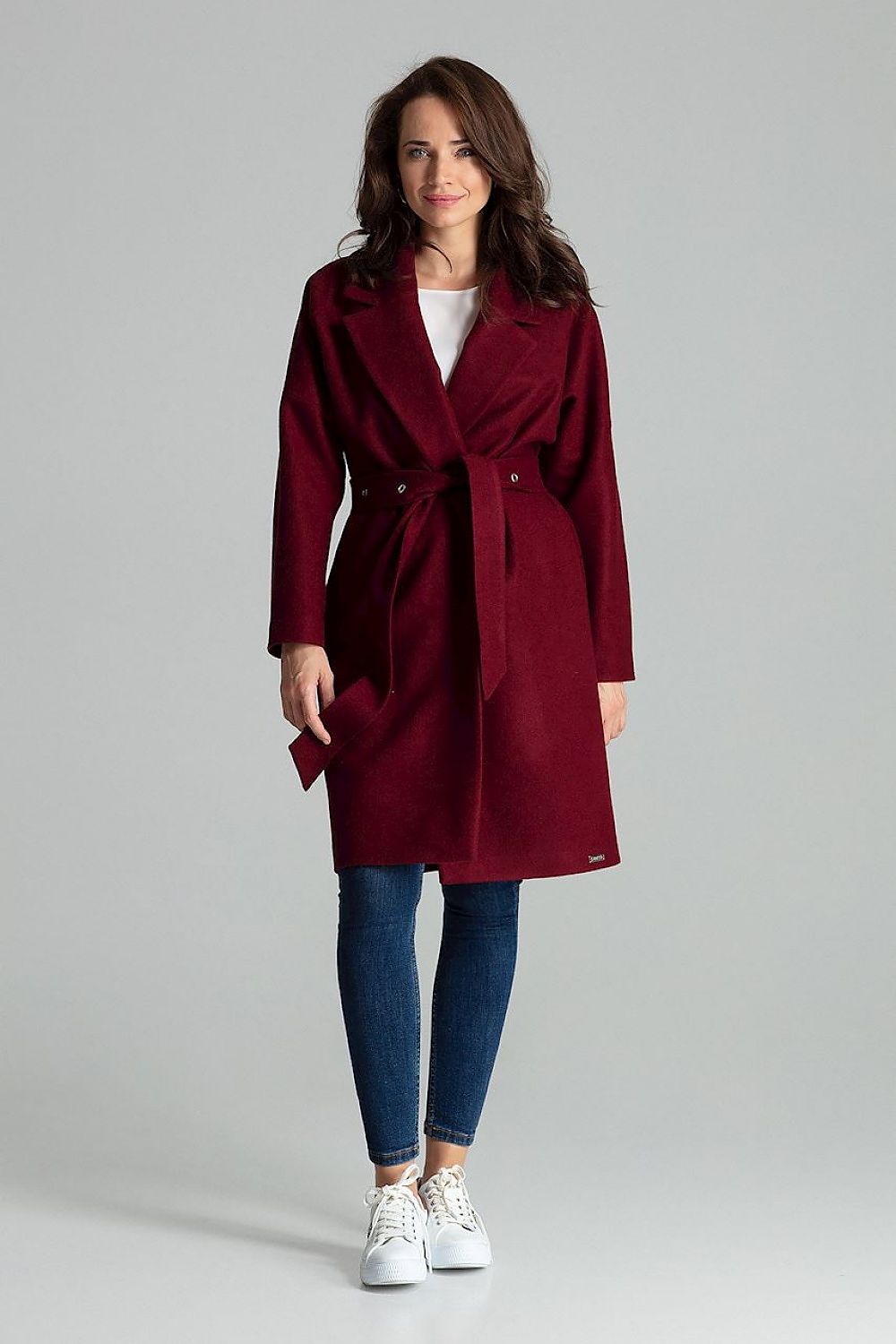 Woman wearing Carivelle Maroon Belted Coat with Wide Lapels, featuring metal eyelets and side-seam pockets, styled with jeans and sneakers.