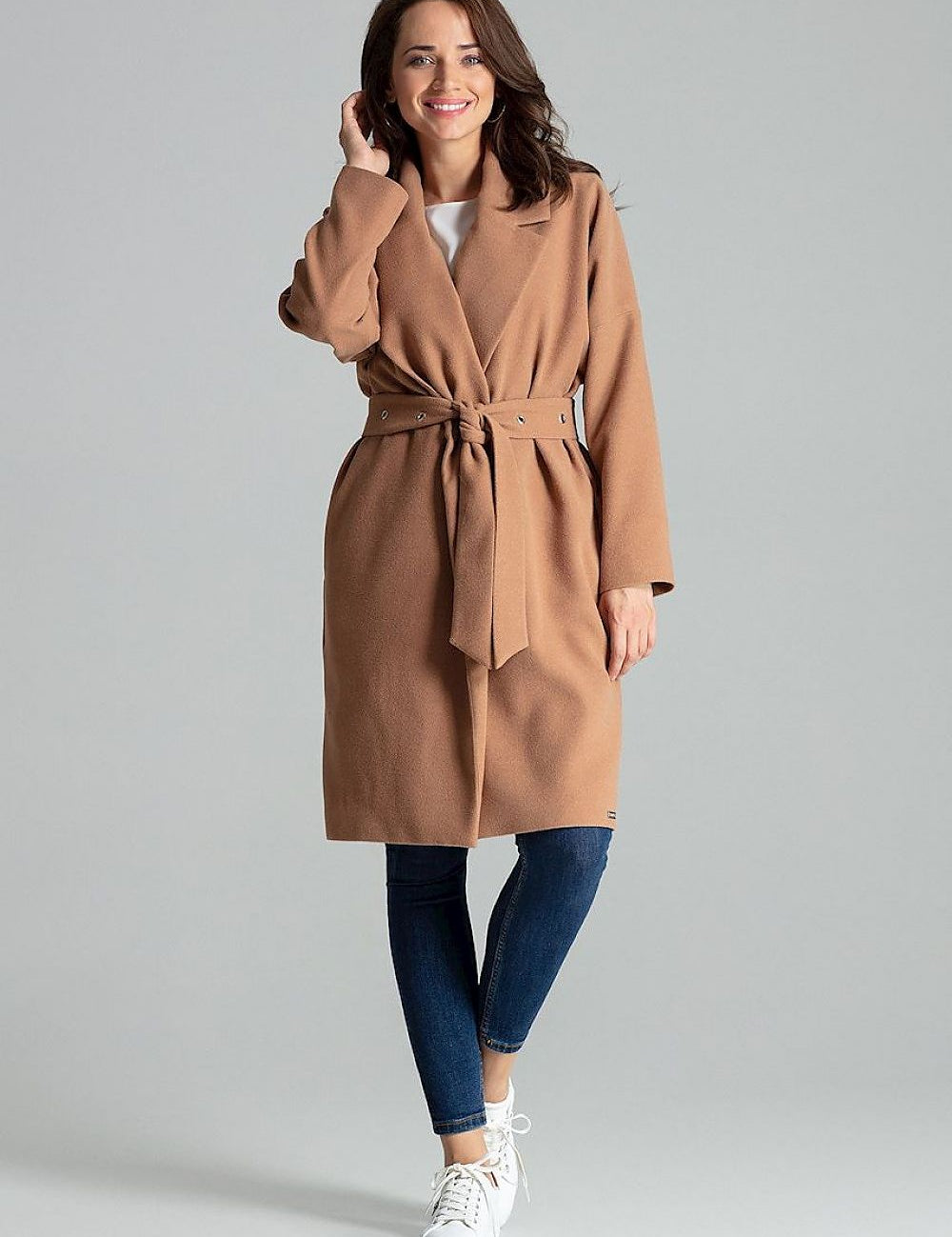 Woman wearing a tan belted coat with wide lapels and jeans, showcasing a stylish casual outfit.