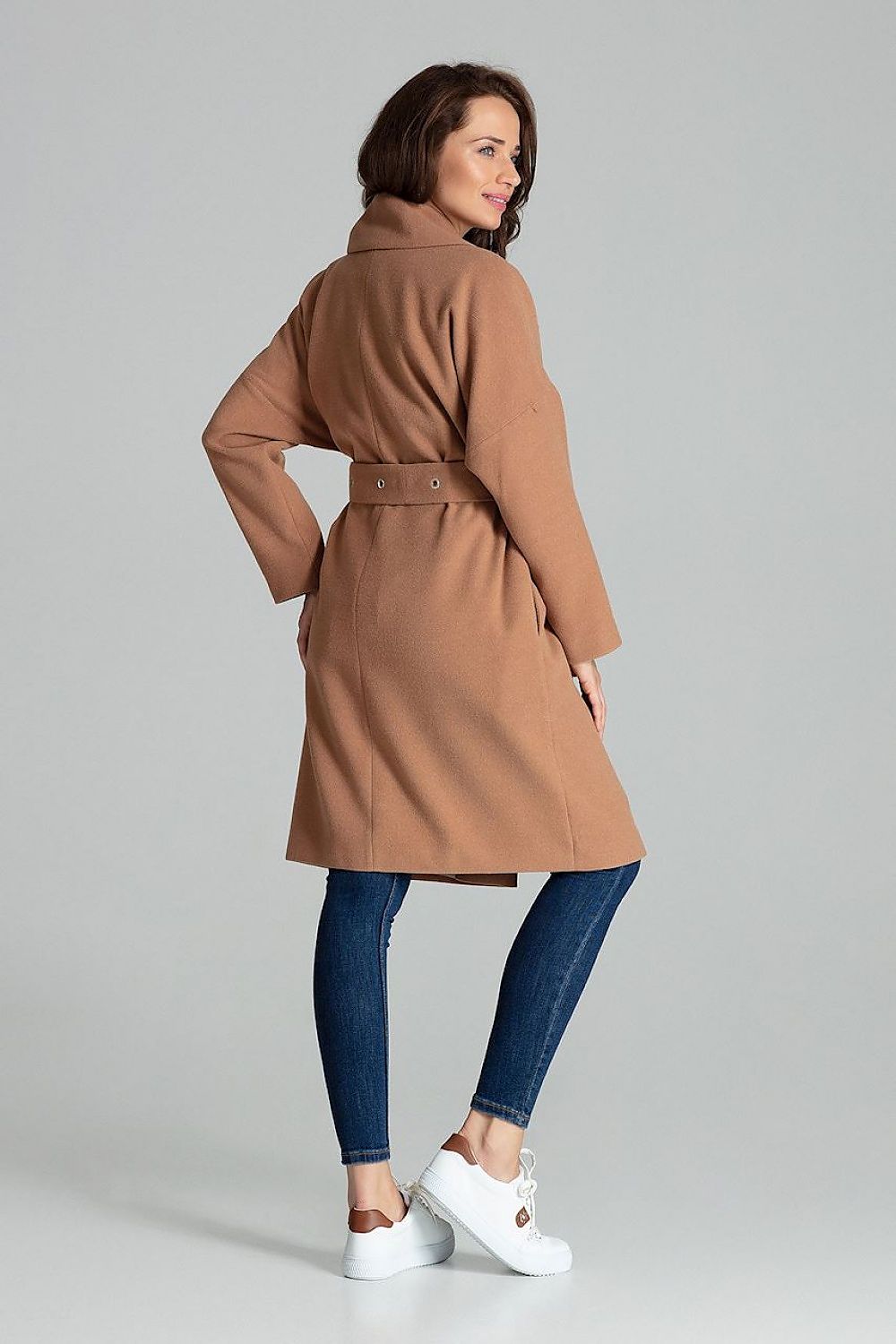 Back view of a woman wearing a stylish brown belted coat with wide lapels, paired with jeans and white sneakers.