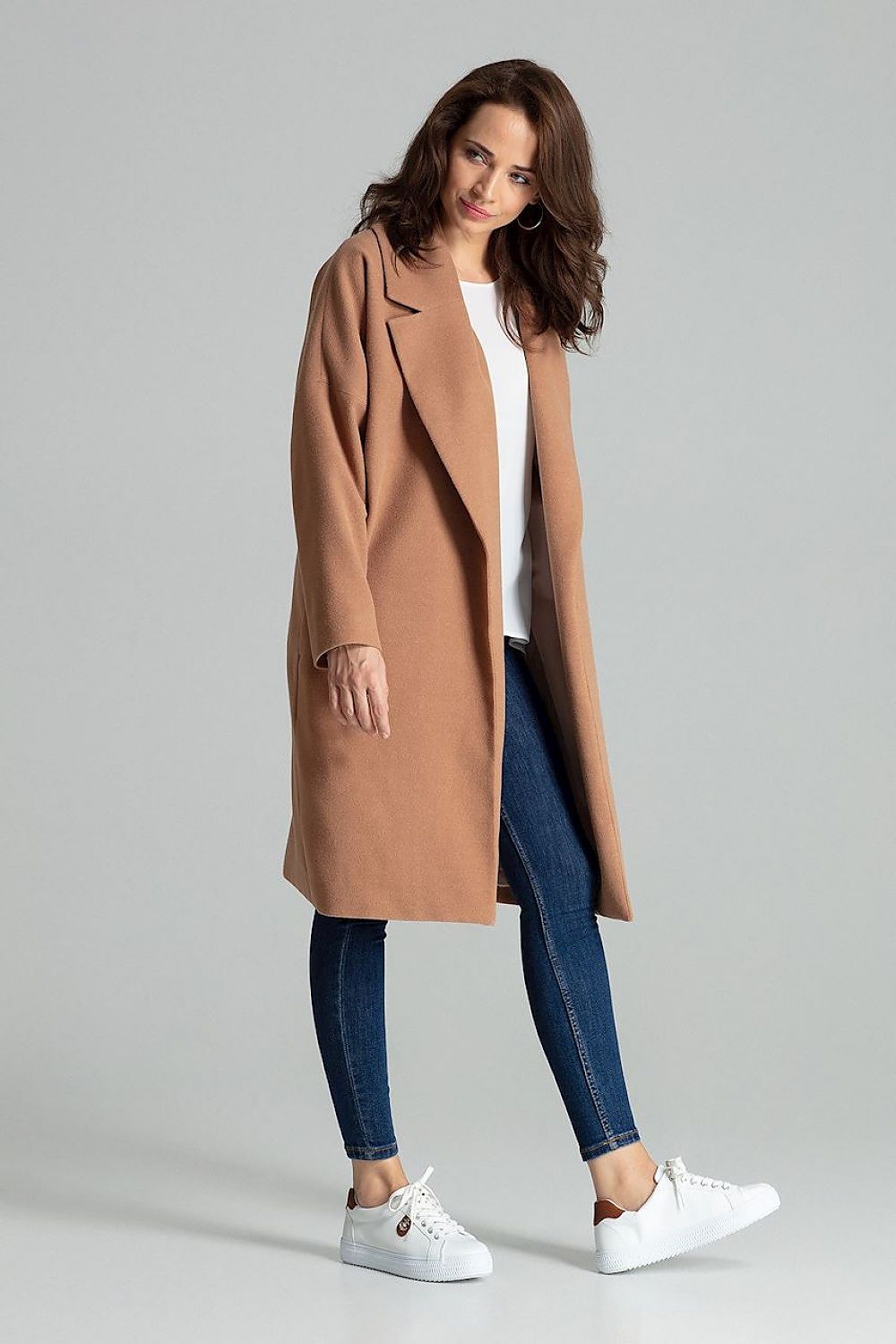 Woman wearing a stylish brown long coat with wide lapels, paired with jeans and white sneakers.