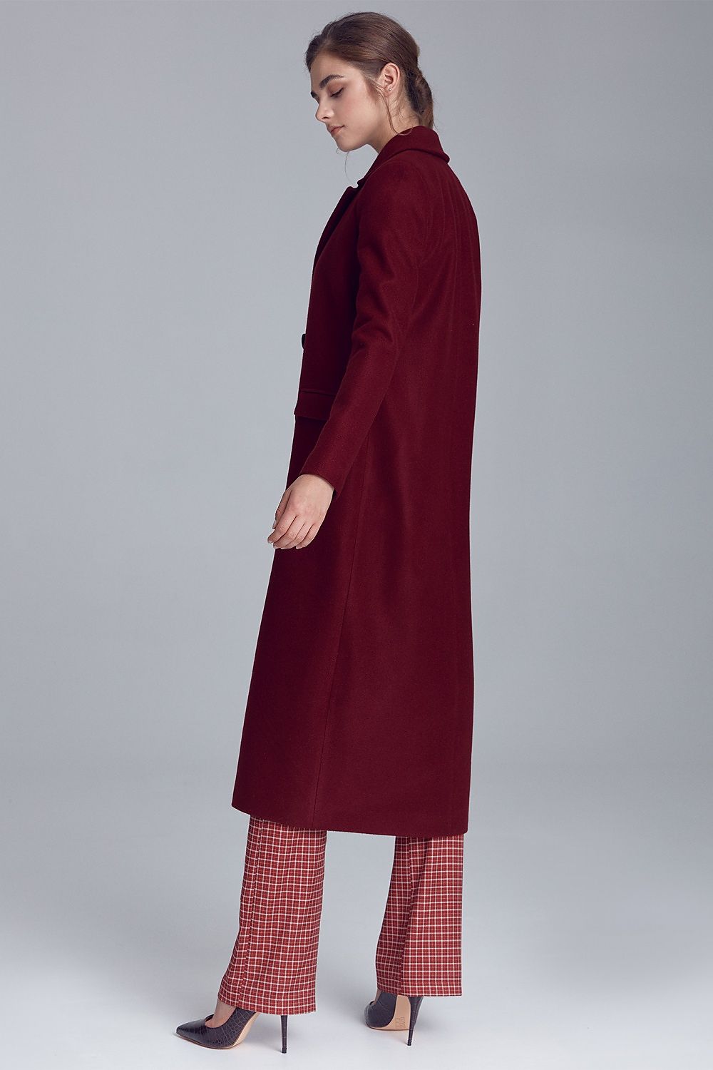 Model wearing Marcelaine long double-breasted wool-blend coat in burgundy, showcasing side profile with classic collar and elegant design.