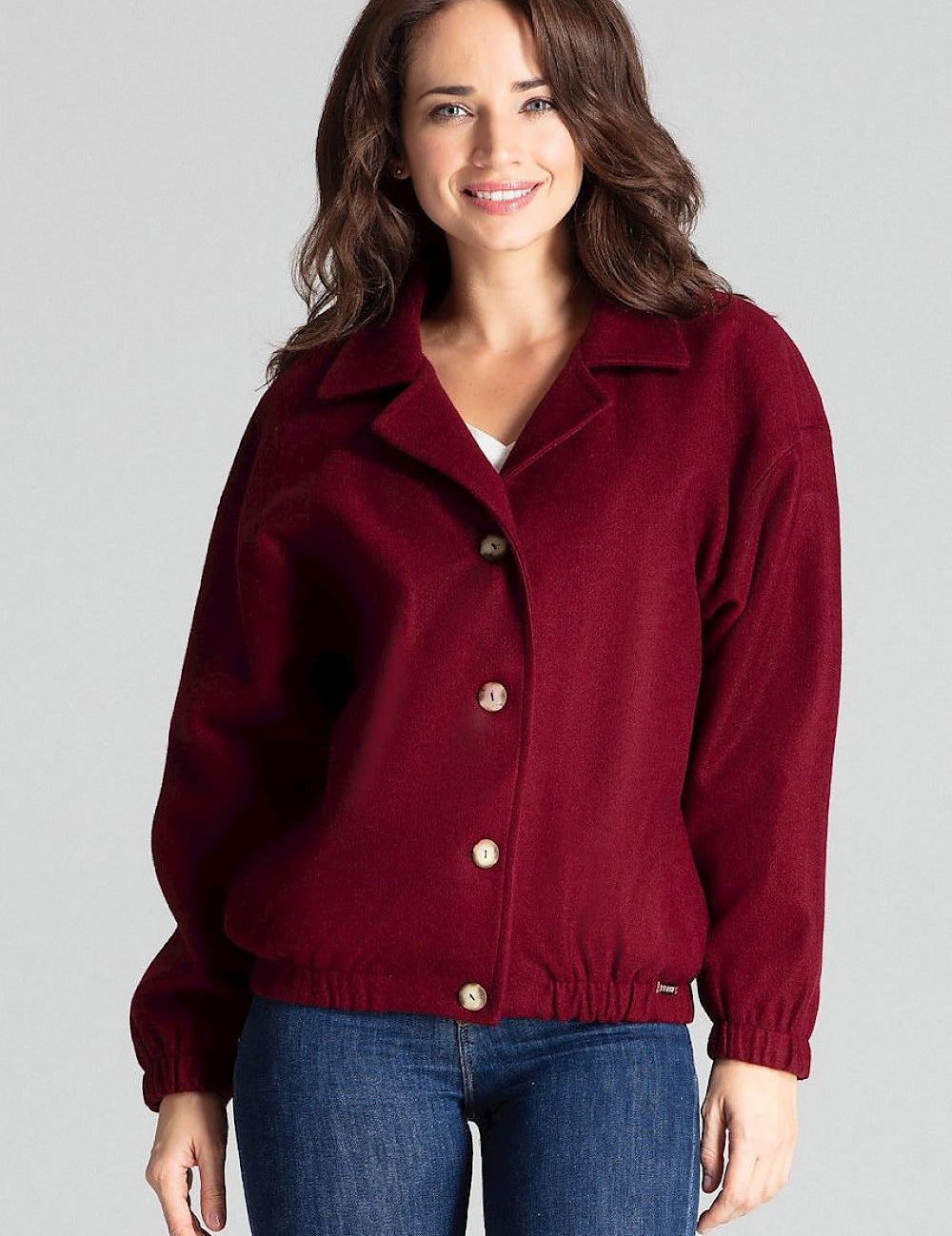 Woman wearing a burgundy loose-fit jacket with decorative buttons and elastic cuffs, styled with jeans for a casual look.