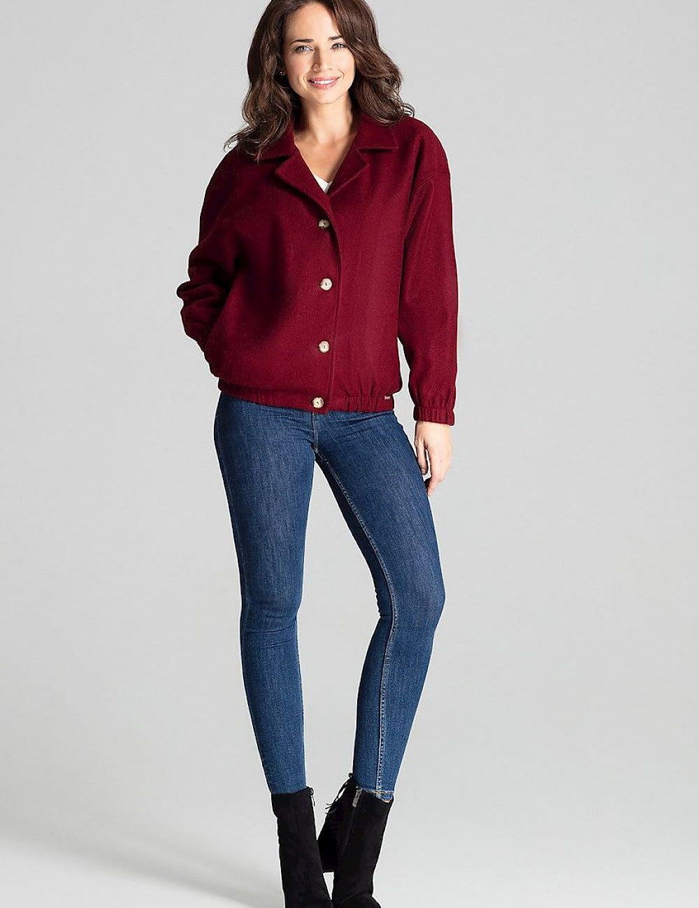 Woman wearing a short red loose-fit jacket with dropped sleeves, stylishly paired with jeans and ankle boots for a chic casual look.