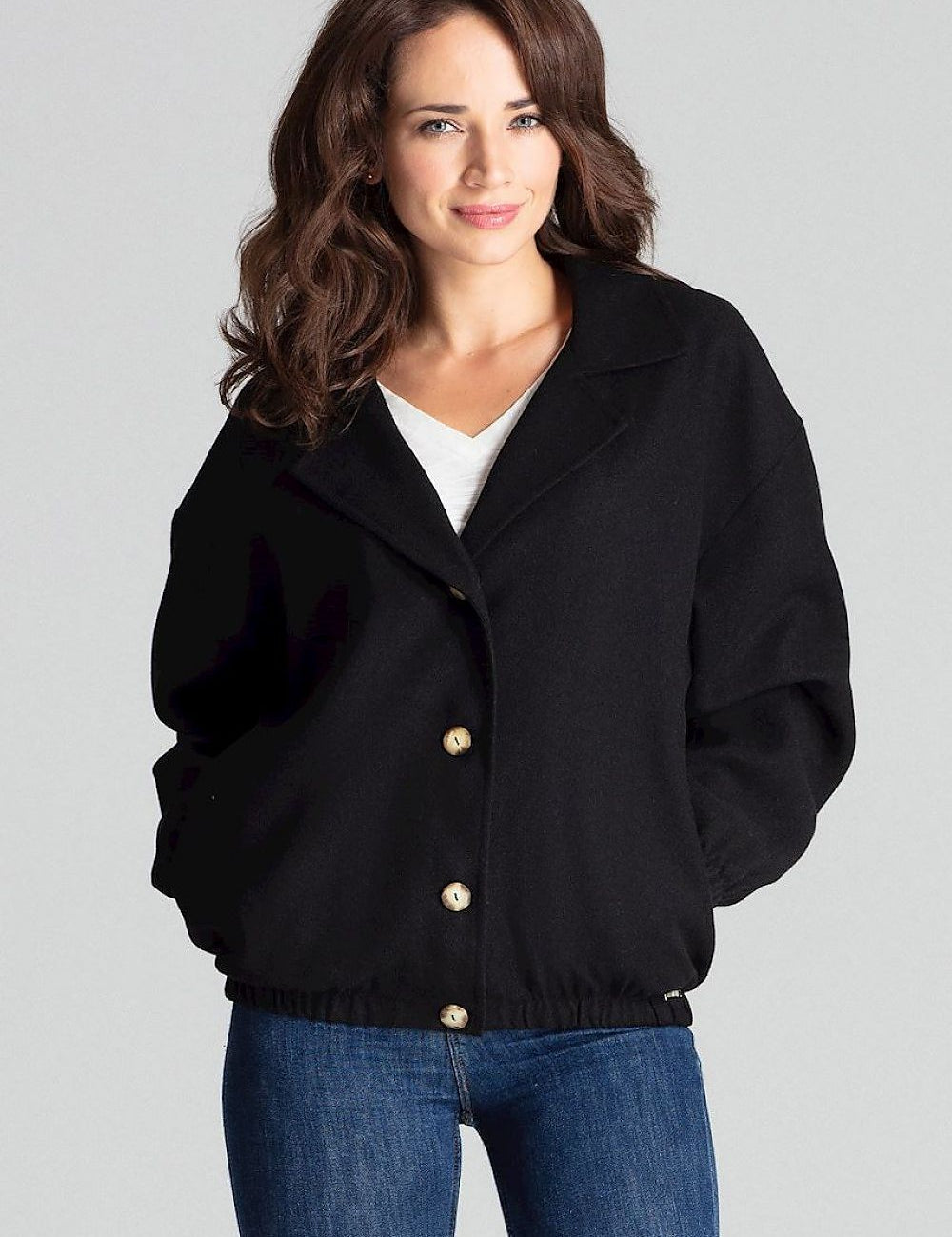 Woman wearing Cerythra short grey loose-fit jacket with decorative buttons and elasticated cuffs, styled casually with jeans.