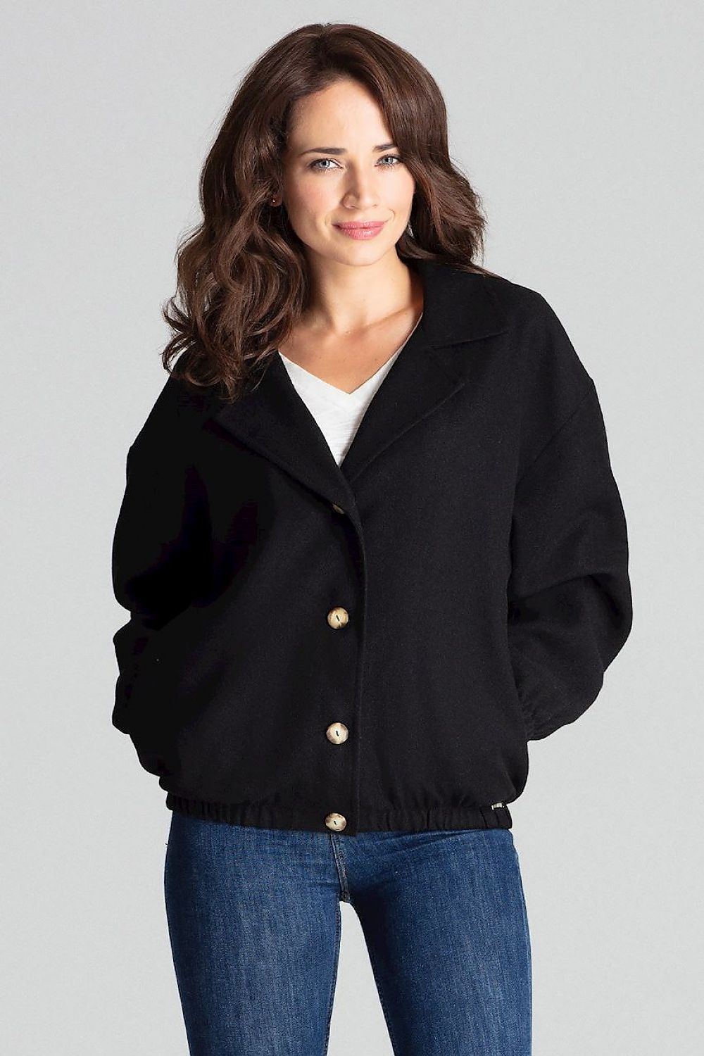 Woman wearing Cerythra short grey loose-fit jacket with decorative buttons and elasticated cuffs, styled casually with jeans.