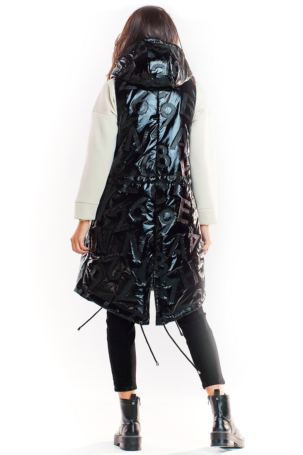 Black shiny quilted hooded gilet vest with extended back hem, stylishly layered over casual attire, featuring side pockets.