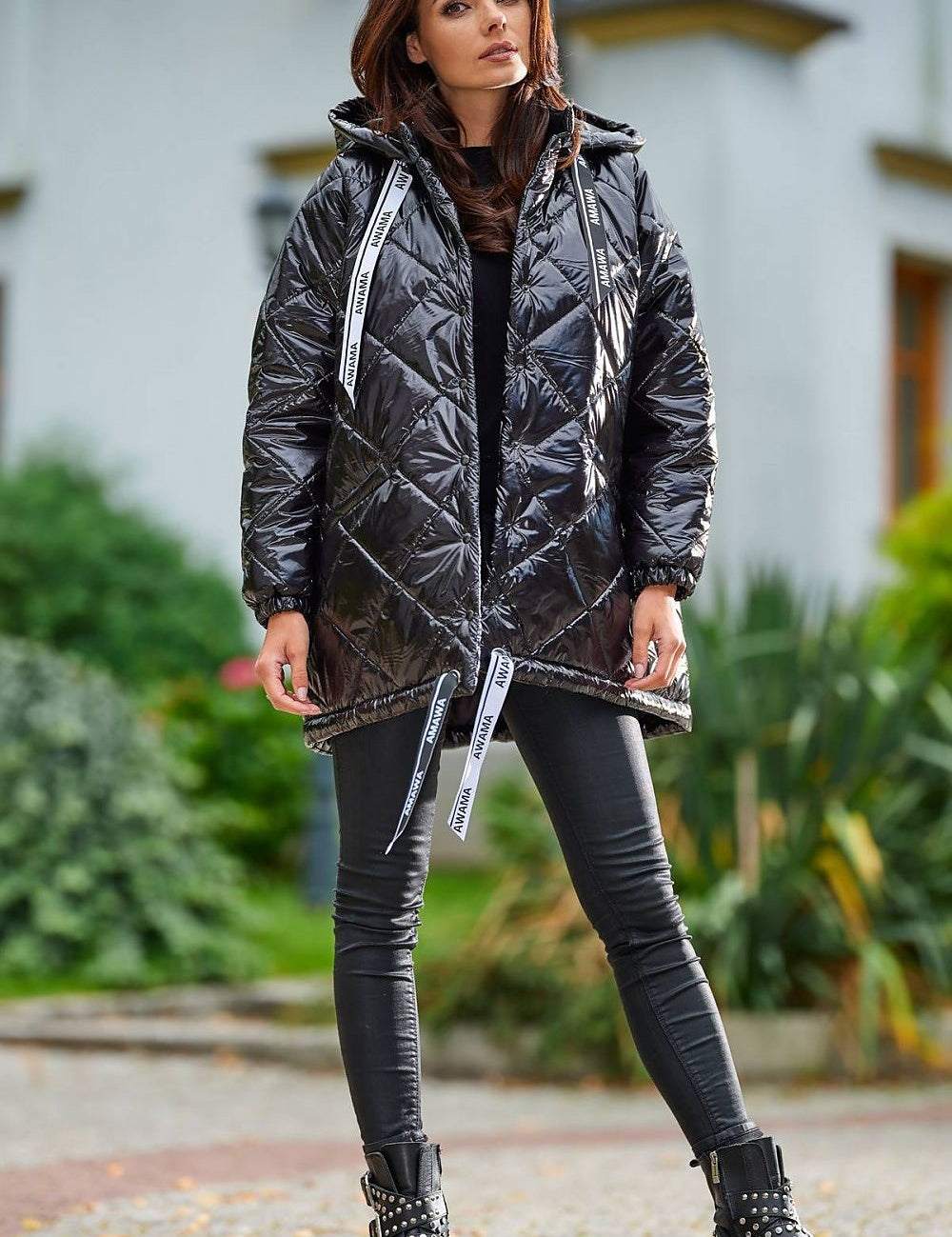 Model wearing Amawa oversized quilted hooded jacket with snap fastening and adjustable logo tape, styled with black pants and boots.