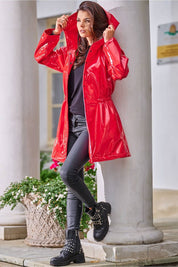 Woman wearing Orlavenne knee-length red vinyl hooded coat with drawstring waist, styled for rain protection and fashion.