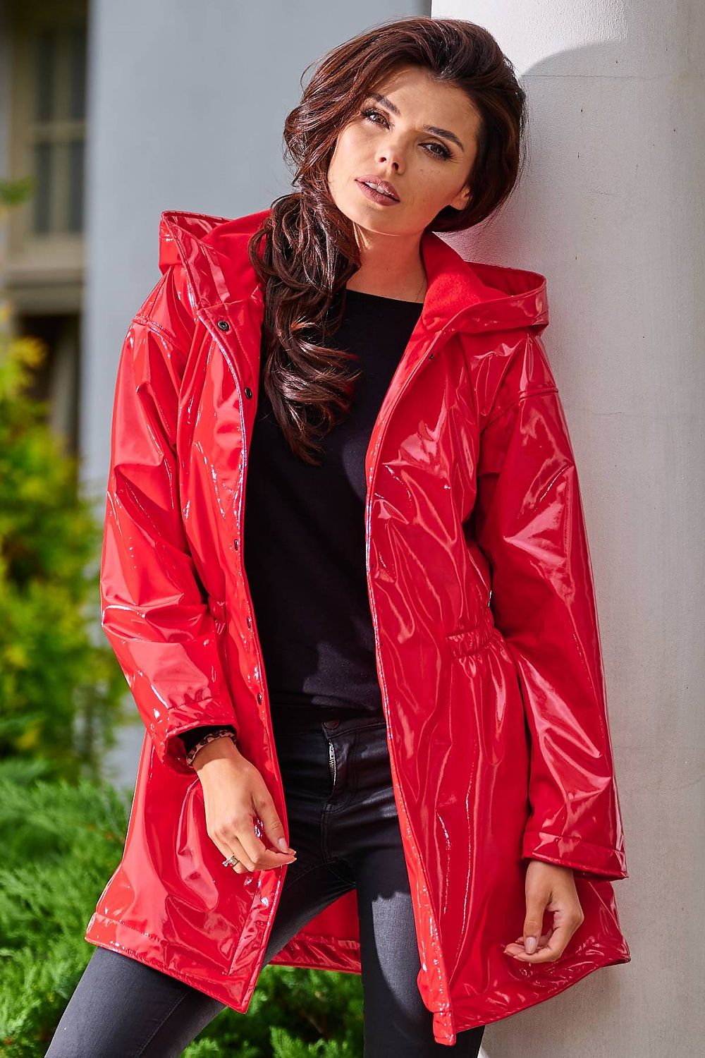 Woman wearing red Orlavenne knee-length vinyl hooded coat, showcasing adjustable fit and rain protection, perfect for transitional seasons.