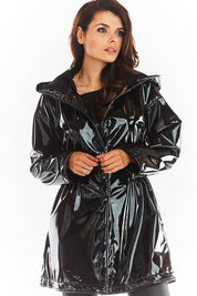 Woman wearing Orlavenne knee-length black vinyl hooded coat with button fastening, showcasing flared hem and adjustable drawstring waist.