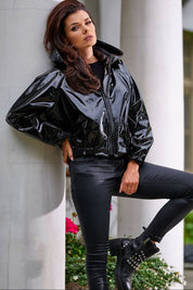 Woman wearing a black Nerivelle short vinyl hooded jacket with ribbed cuffs, standing outdoors, showcasing street style fashion.