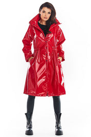 Woman wearing a red Marveena knee-length vinyl raincoat with high collar and straight sleeves, styled for modern weather protection.