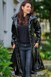 Woman wearing Marveena knee-length black vinyl raincoat with high collar and flared hem, standing outdoors.