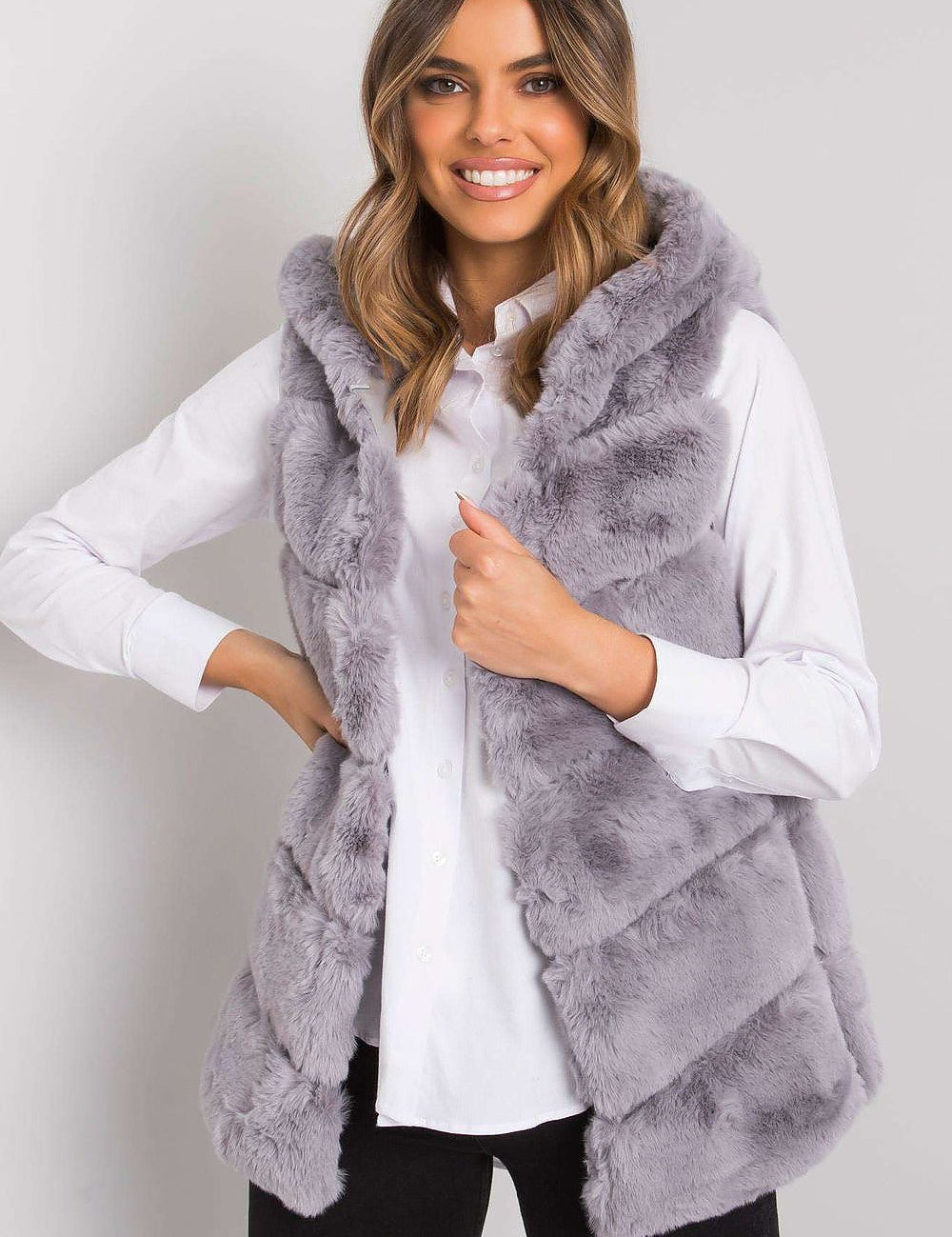 Woman wearing gray faux fur vest over white shirt, smiling.