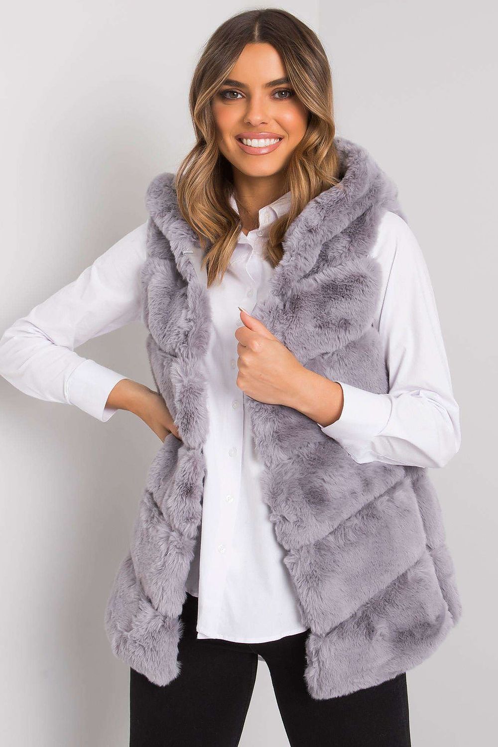 Woman wearing gray faux fur vest over white shirt, smiling.